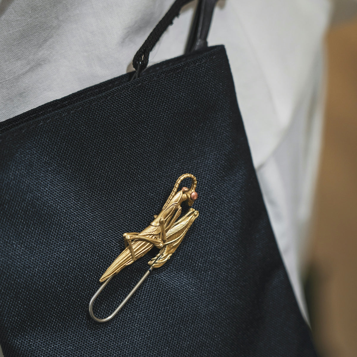 a person holding a black bag with a gold bird pin on it