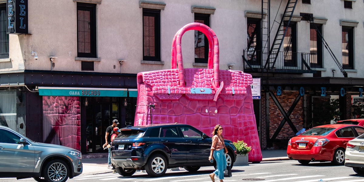 A woman crossing the street in front of a pink bag