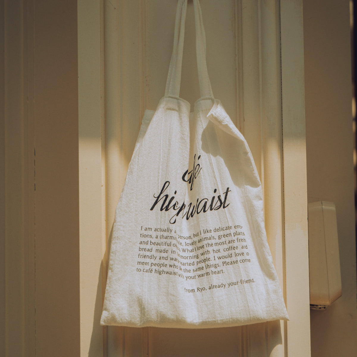 A white tote bag hangs on a door.