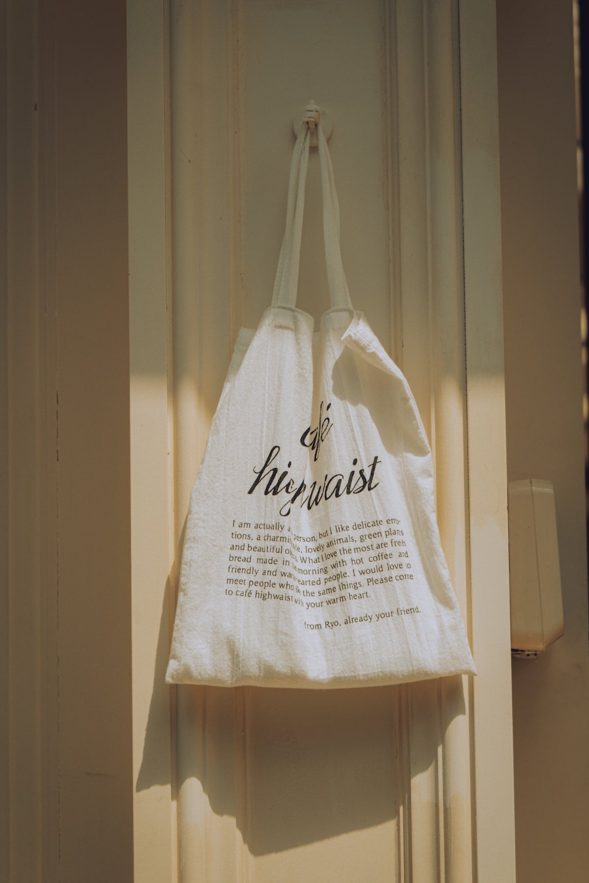 A white tote bag hangs on a door.